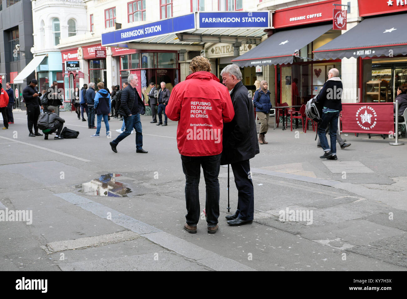 Red Cross charity worker and man talk in street to collect donations in front of Farringdon Railway Station sign in London England UK   KATHY DEWITT Stock Photo