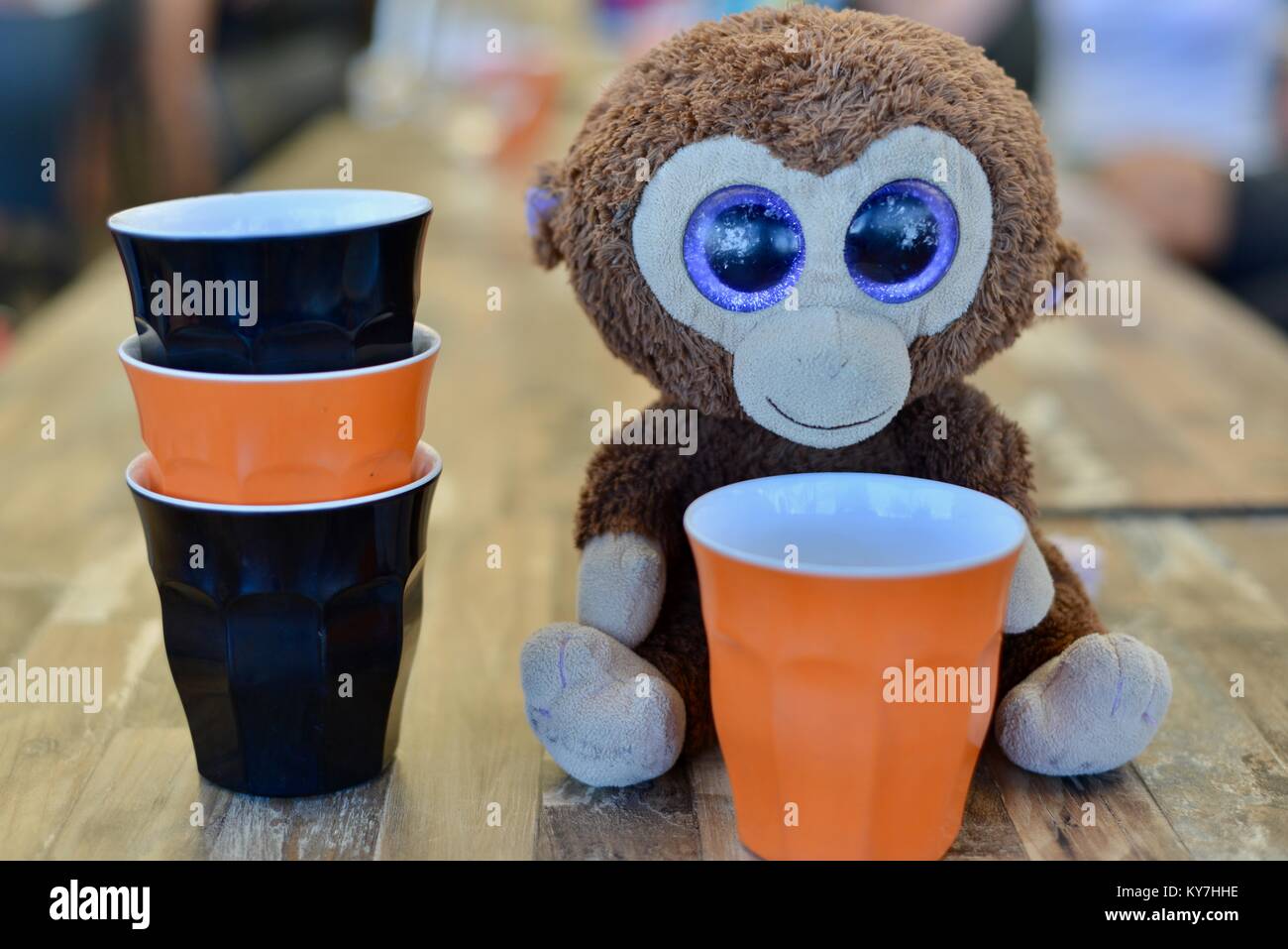 Big eyed toy monkey sitting on a cafe table among an arrangement of   of black and orange plastic cups, Sunshine coast, Queensland, Australia Stock Photo