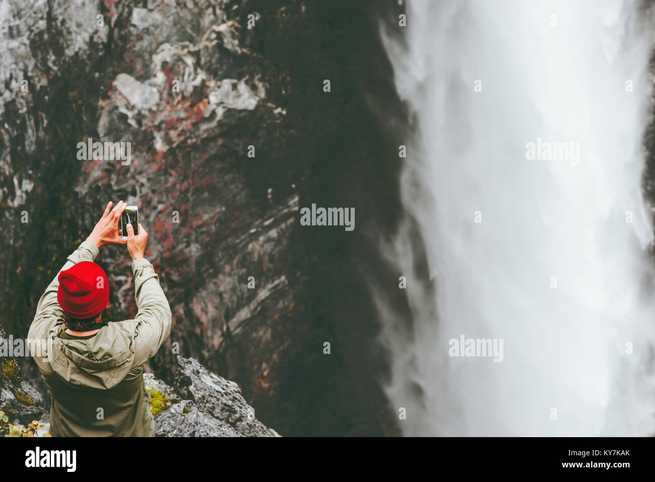 Traveling Man taking photo of Vettisfossen waterfall using smartphone on cliff adventure lifestyle concept extreme vacations outdoor wanderlust Stock Photo