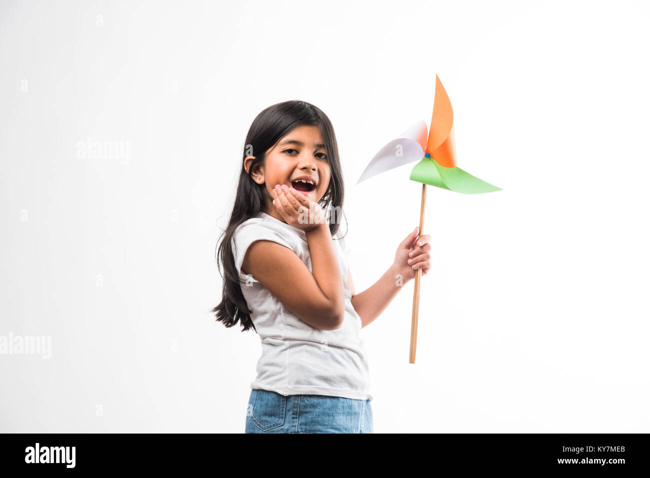 indian girl with paper windmill toy made up of tricolour or indian flag colours. Saluting, looking at camera or with red heart toy, celebrating 26 Jan Stock Photo