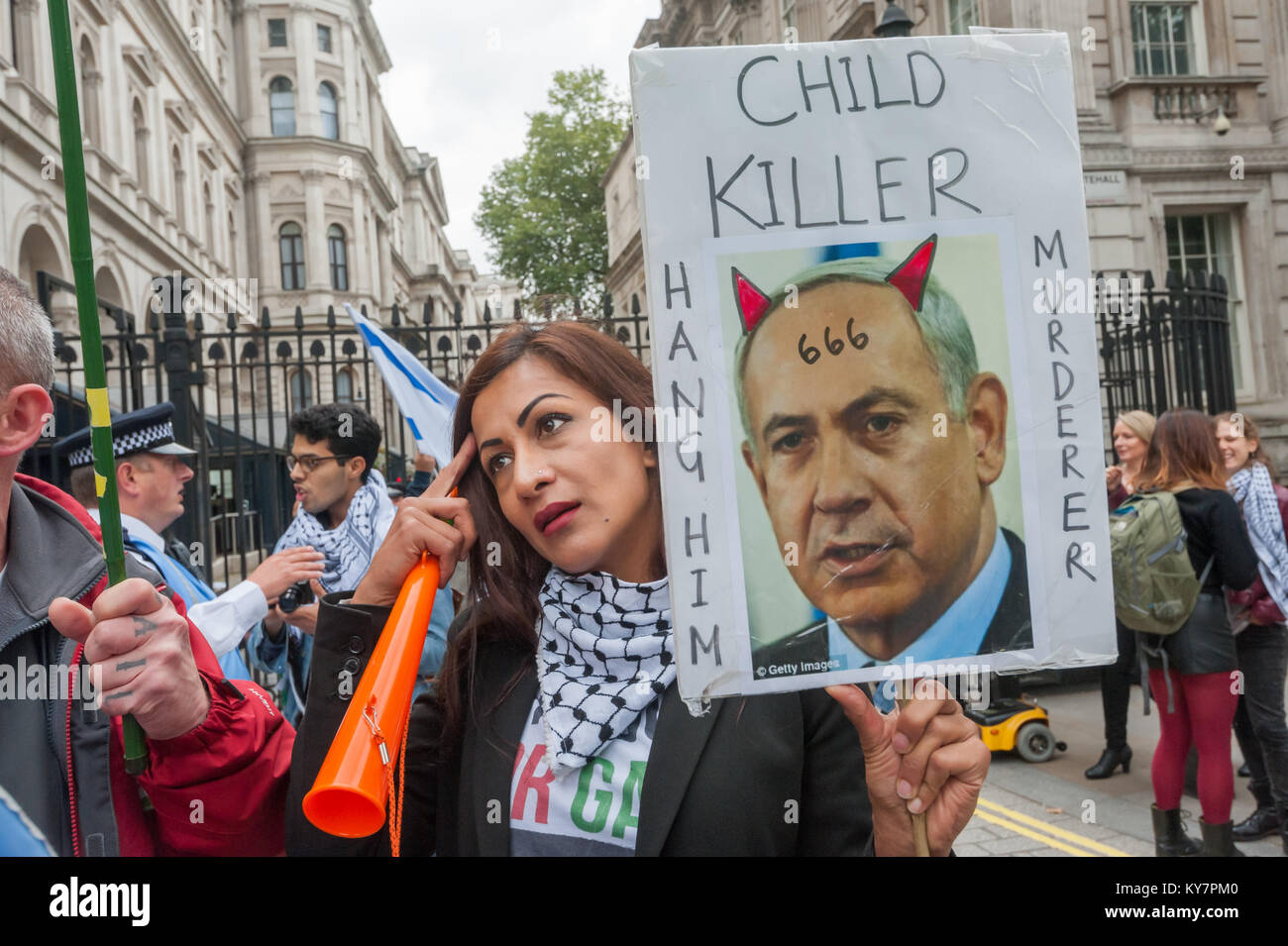 A woman holds a poster shoing Netianyahu withe the Devil's horns and the number 666 on his forehead labelling him as a child killer and mudrerer and urging 'Hang Him' outside Downing St Stock Photo