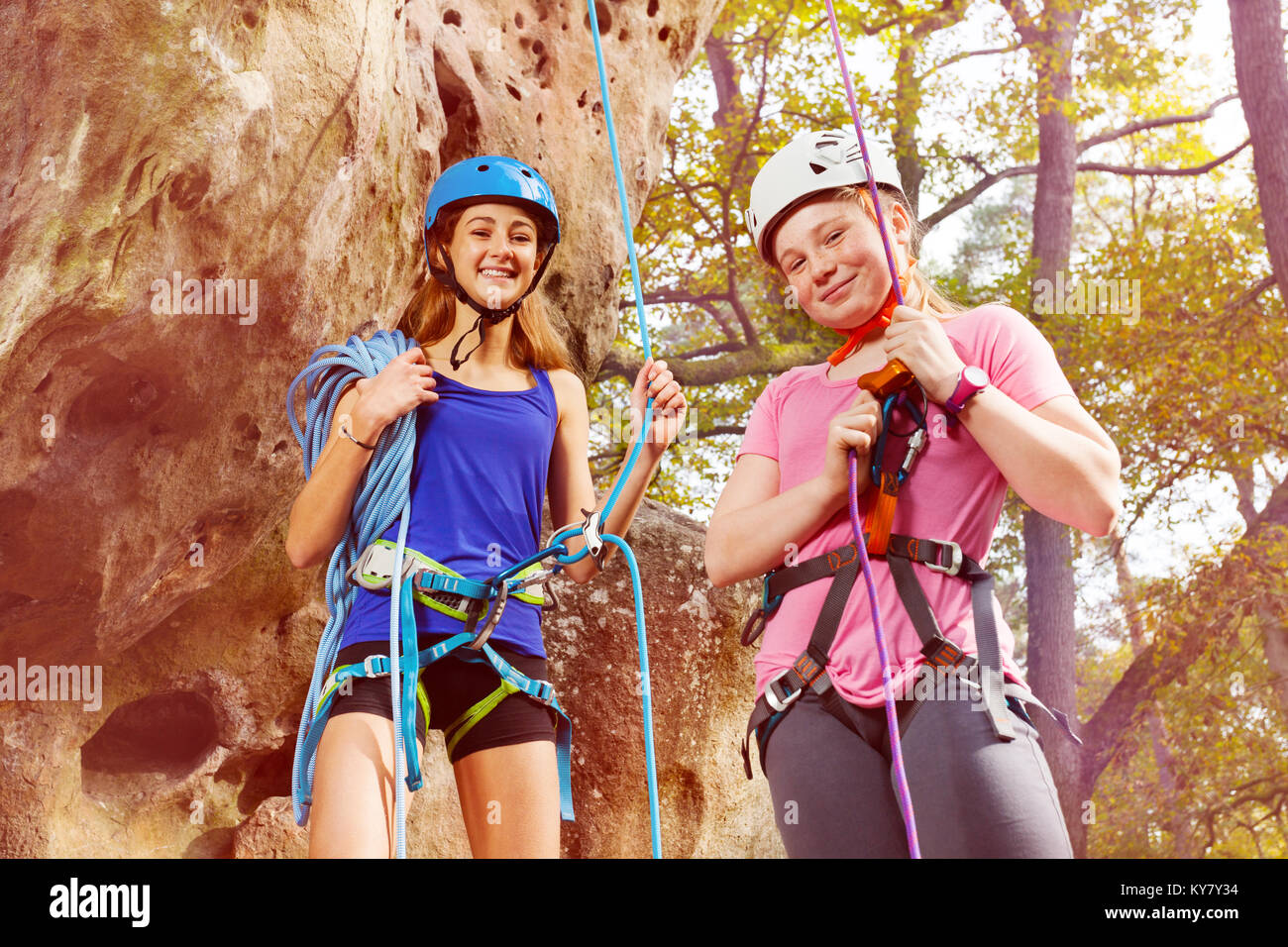 Two happy alpinists, young woman and teenage girl in helmets at the bottom of a mountain Stock Photo