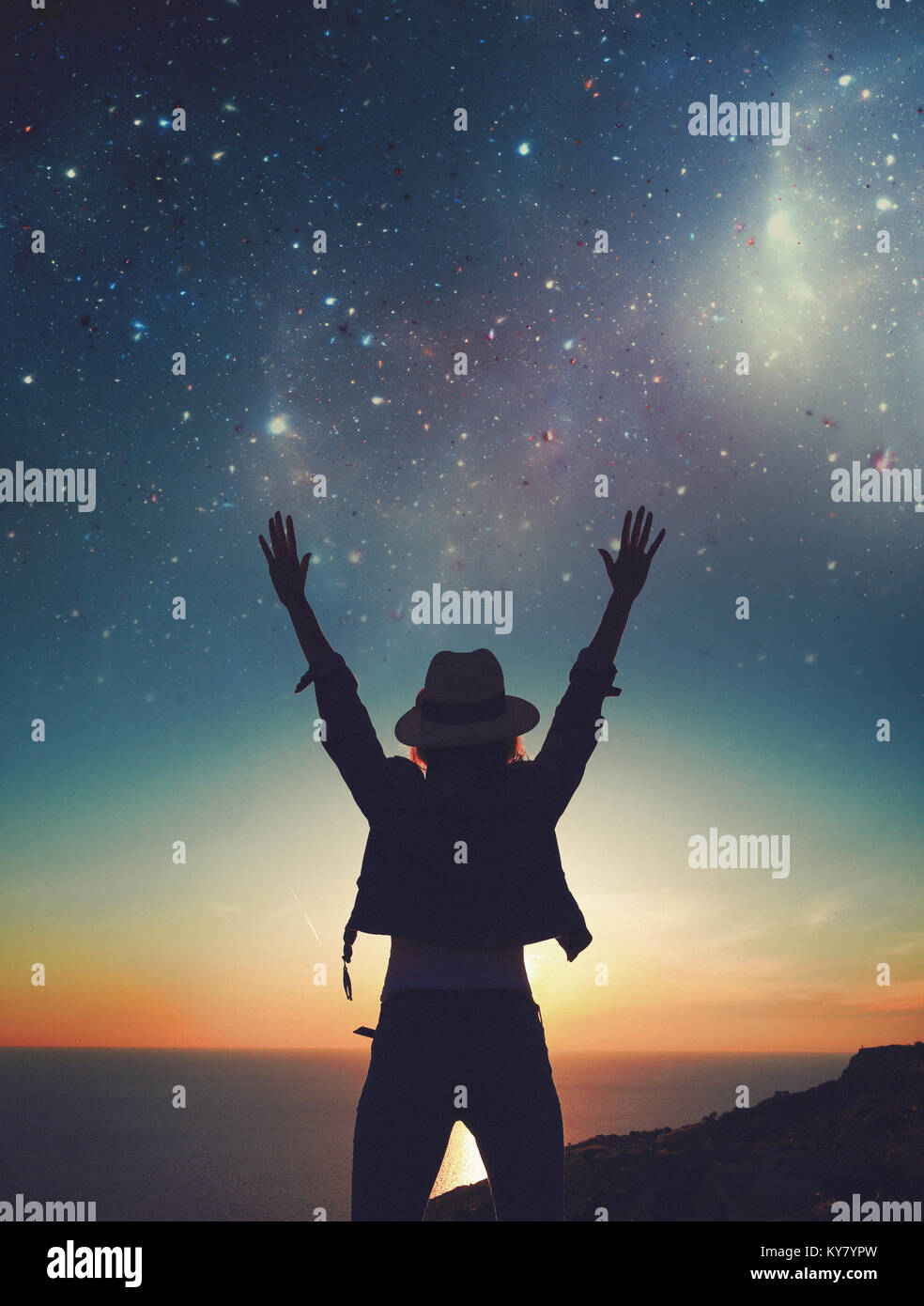 Carefree womans silhouette hands up to the stars on cliff at sea Stock Photo