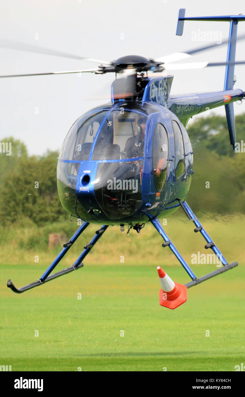 Hughes MD 500 G-RISK helicopter carrying out a trick at an airshow of picking up and moving around a traffic cone on its skid Stock Photo