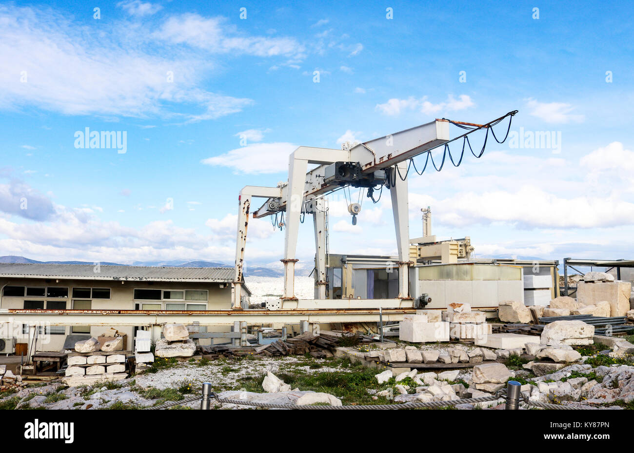 Giant crane on tracks being used to reconstruct Parthenon on Athens Acroplis with pieces of the ruins organized in foreground and Athens and mountians Stock Photo