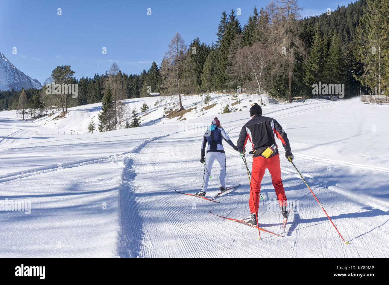 Two cross-country Skiers runs on groomed ski track in sunny winter day. Winter mountain landscape: Tirol, Alps, Austria. Stock Photo