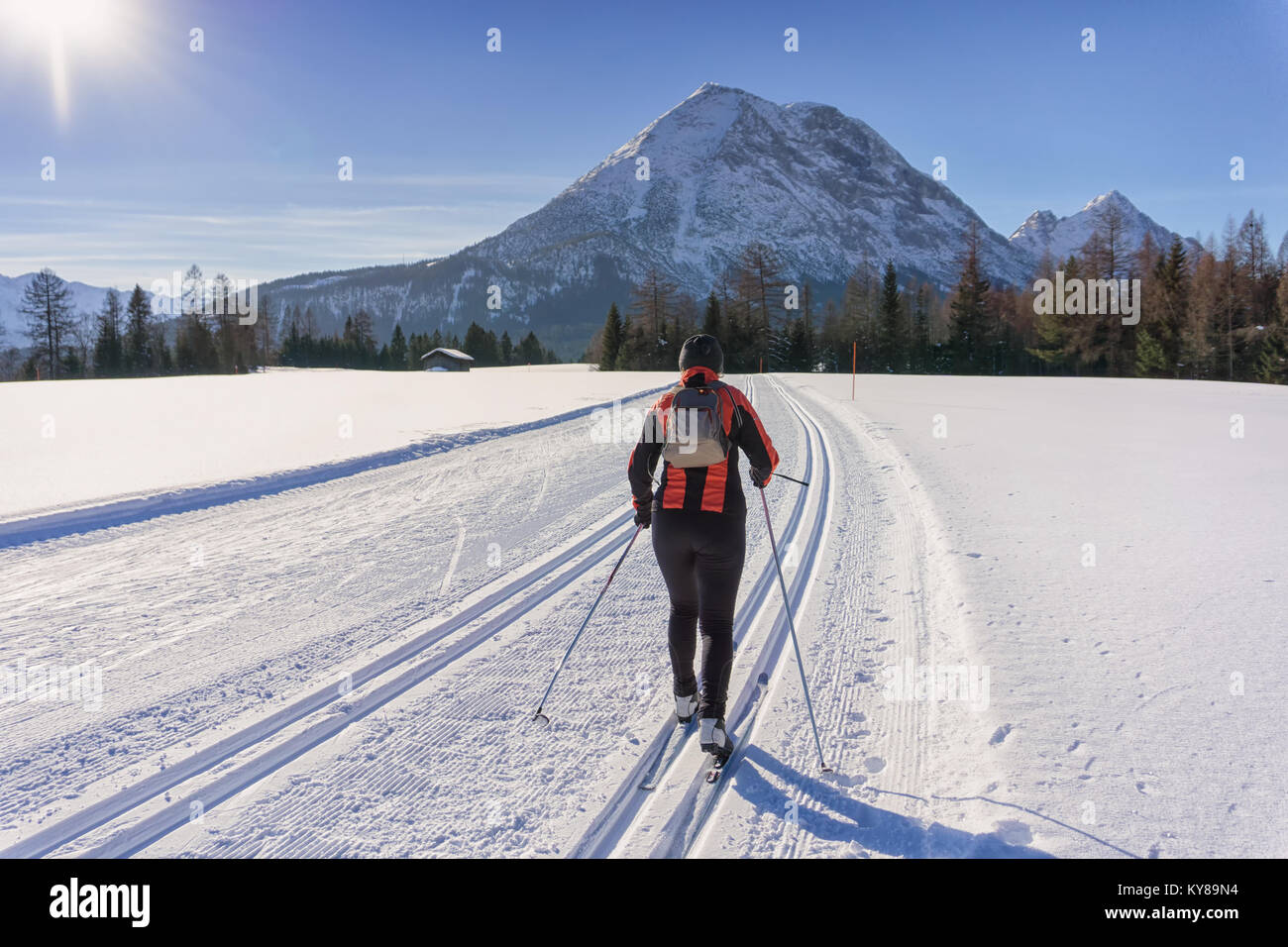 Cross-country Skier in red jacket  runs on groomed ski track in sunny winter day. Winter mountain landscape: Tirol, Alps, Austria. Stock Photo