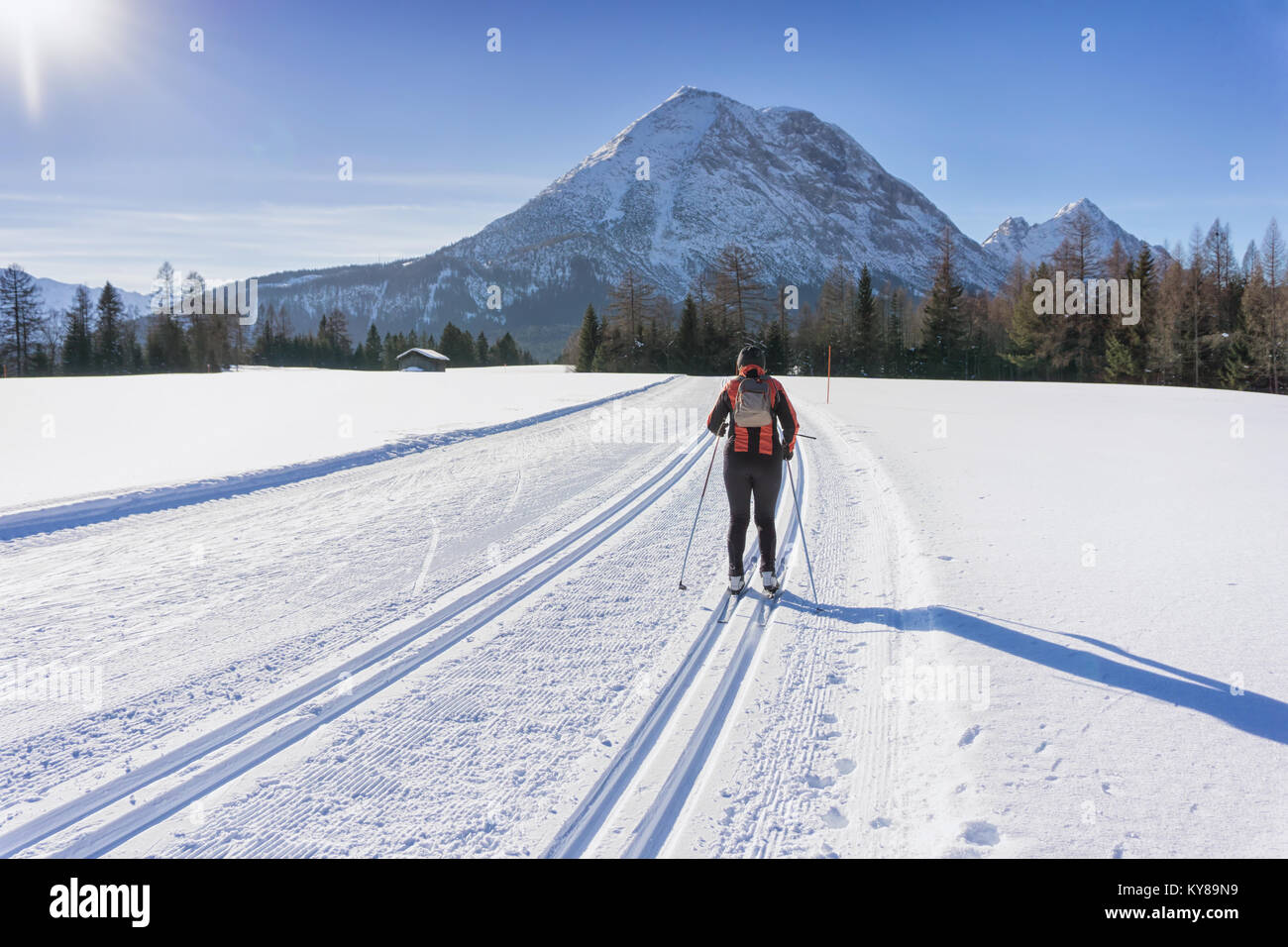 Cross-country Skier in red jacket  runs on groomed ski track in sunny winter day. Winter mountain landscape: Tirol, Alps, Austria. Stock Photo
