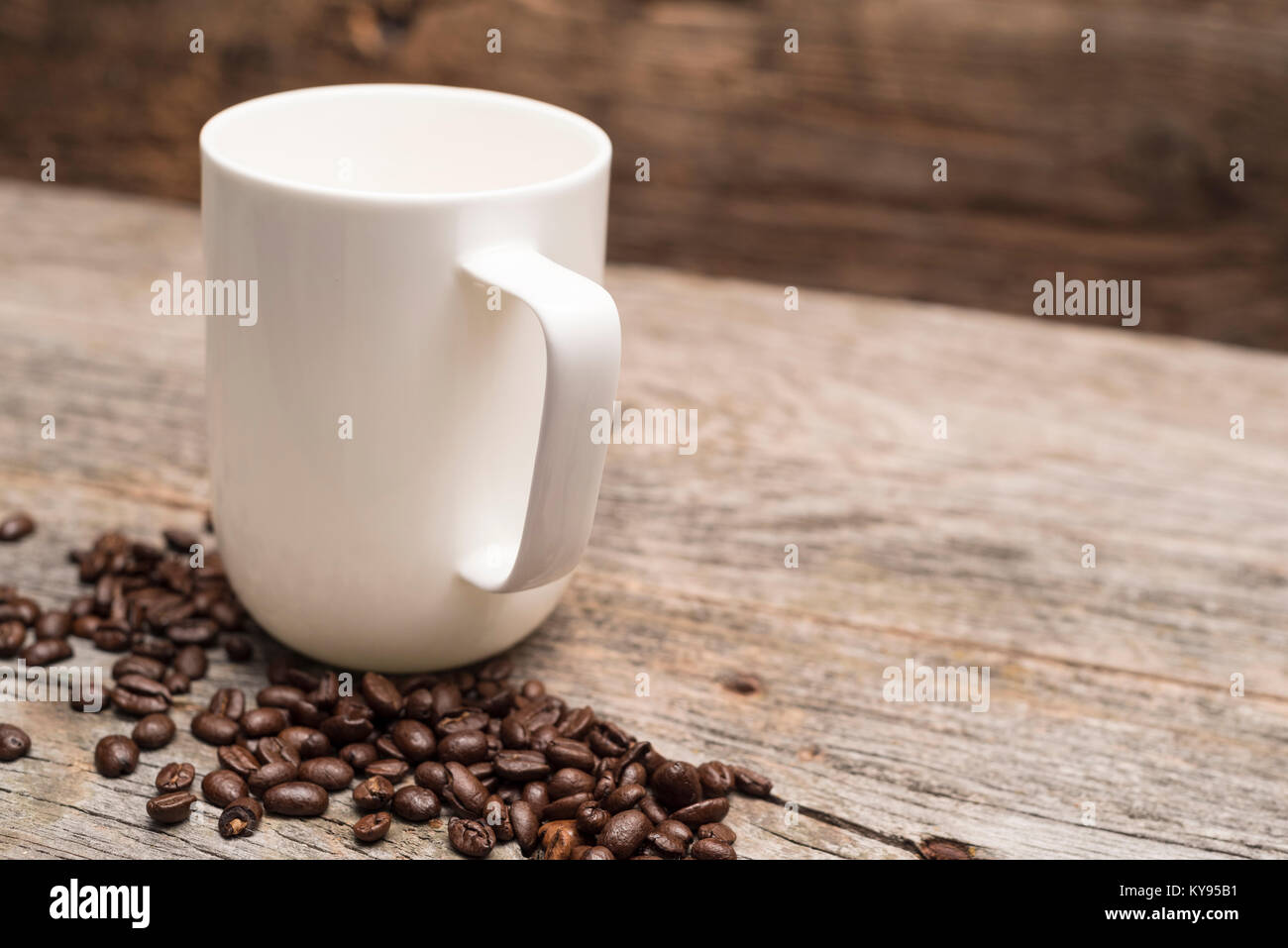 one large white coffee mug surrounded by roasted coffee beans shot against rustic brown barn wood background ready for next pour Stock Photo