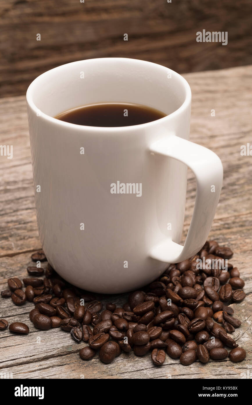 coffee in large white mug surrounded by roasted coffee beans shot against rustic brown barn wood background Stock Photo