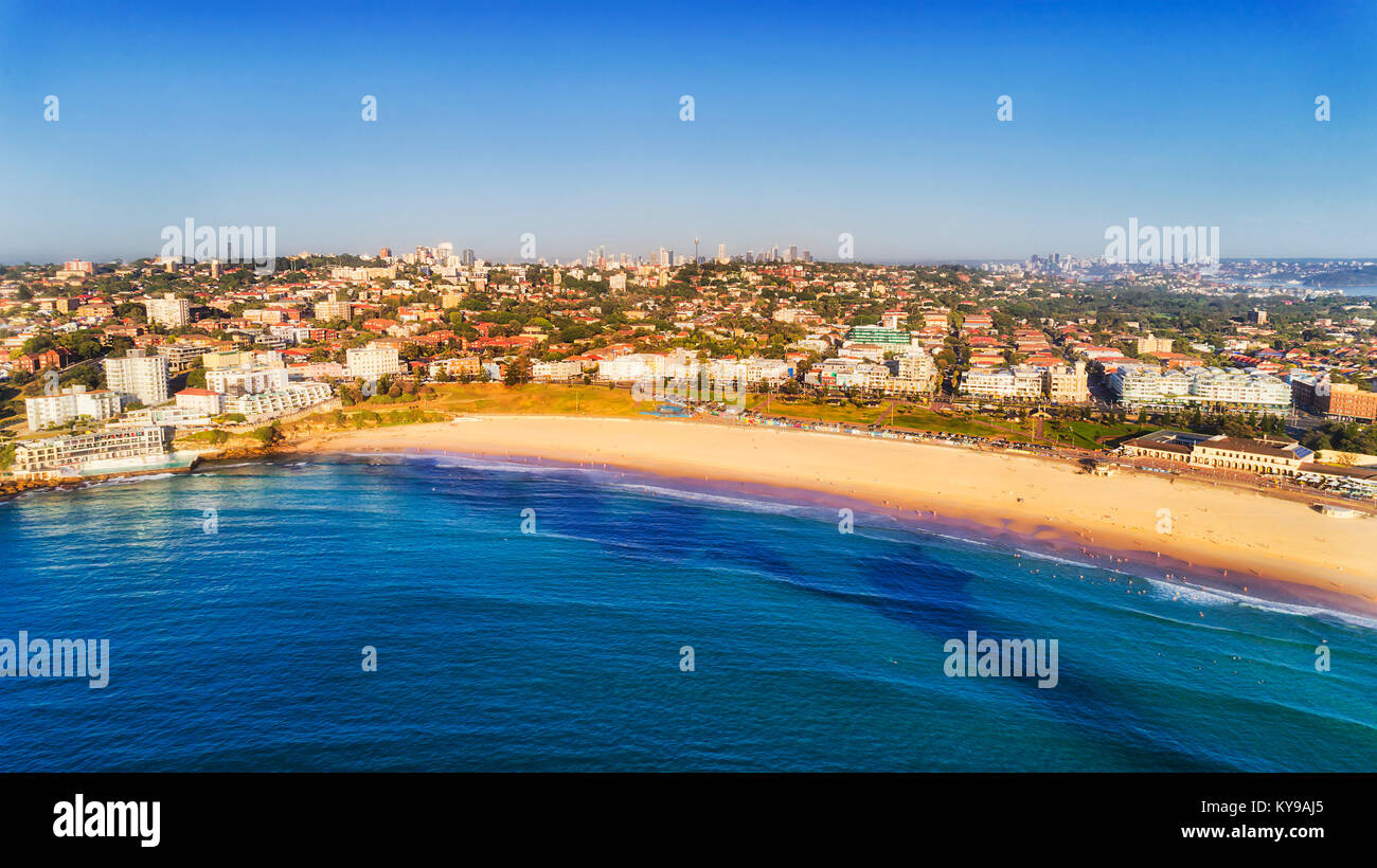 Waterfront of famous Sydney beach Bondi with wide area of clean sand and city CBD towers on the horizon under blue sky on a sunny summer day. Stock Photo