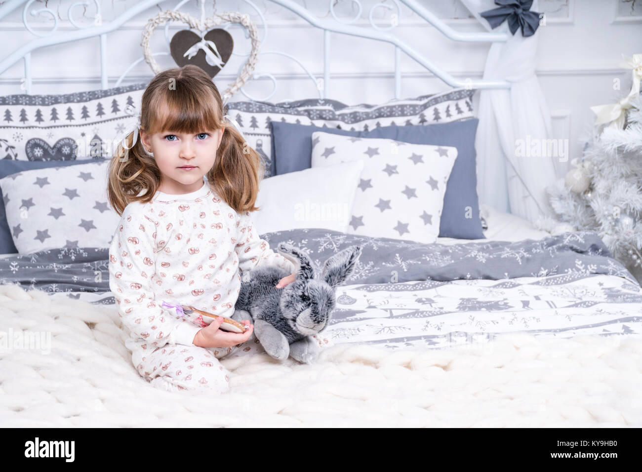 Portrait of a beautiful little girl in pajamas with a toy rabbit in bed ...