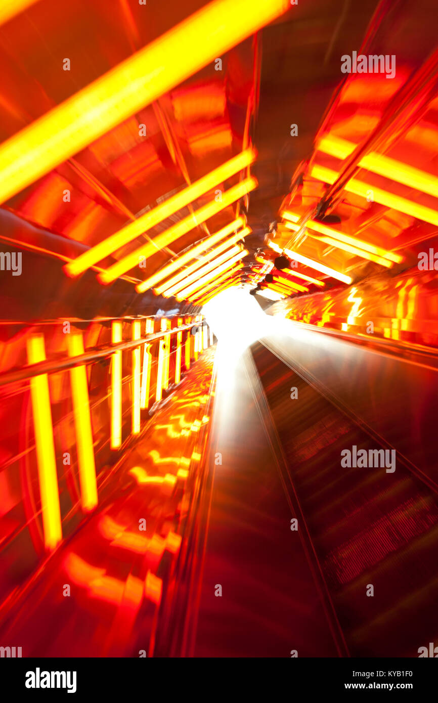 An escalator through a tunnel with red illumination and motion blur. Stock Photo