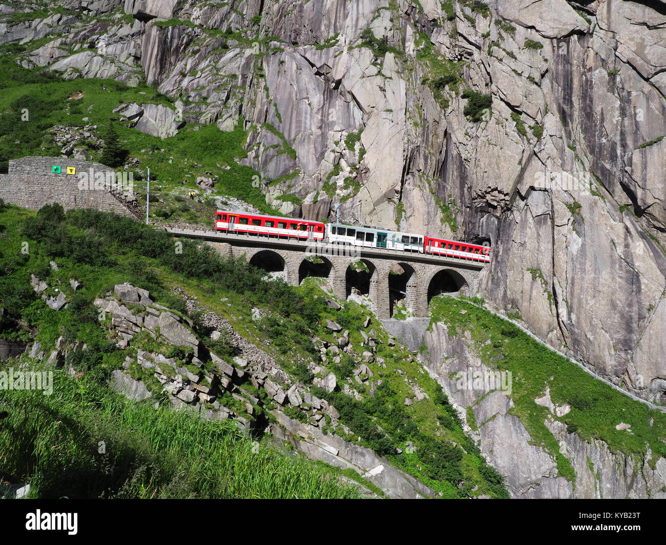 Red express train on scenic stony St. Gotthard railway bridge and tunnel, swiss Alps, SWITZERLAND Stock Photo