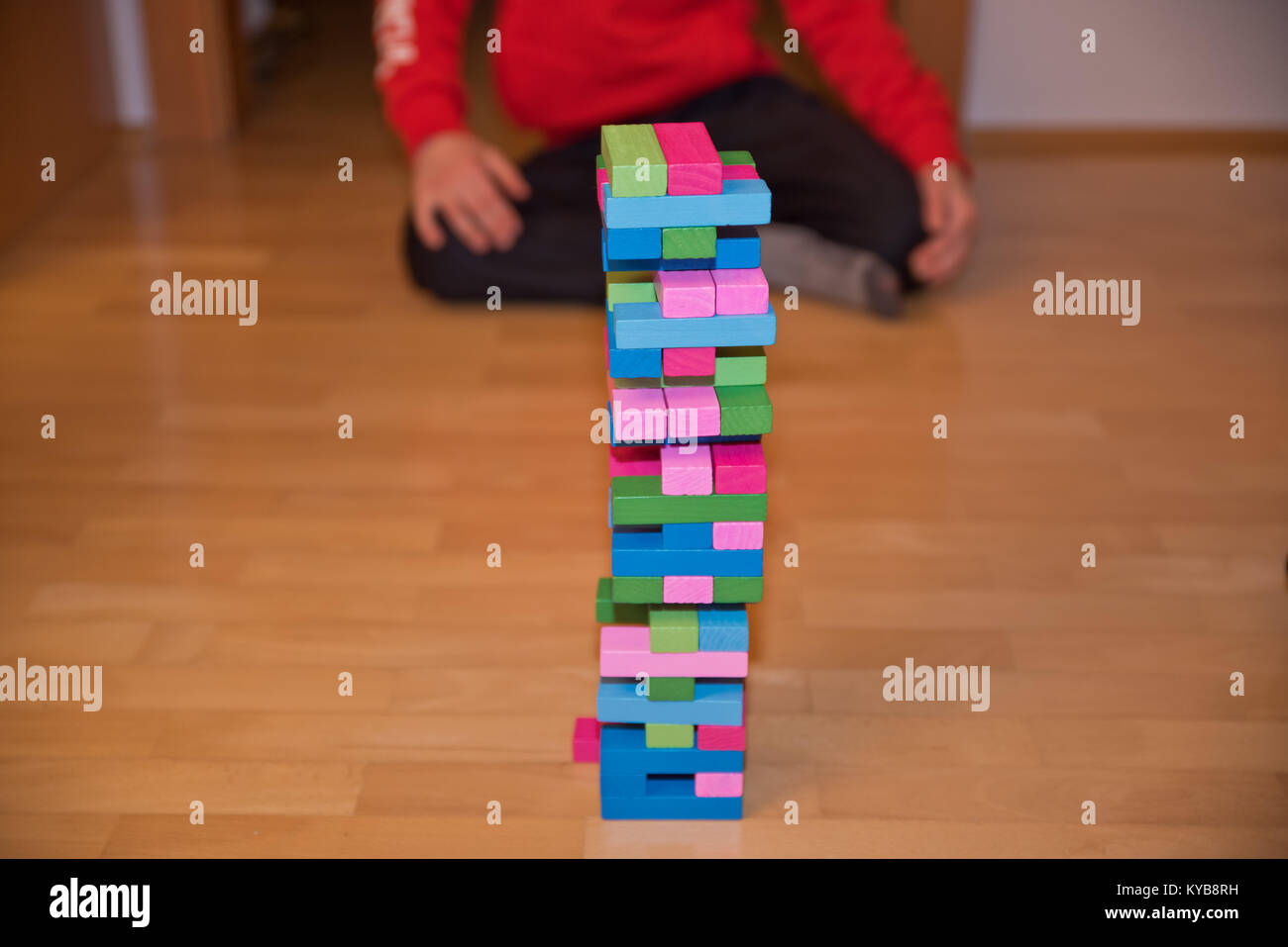 Child sitting behind colorful Jenga tower aka Klodsmajor parlor game, a