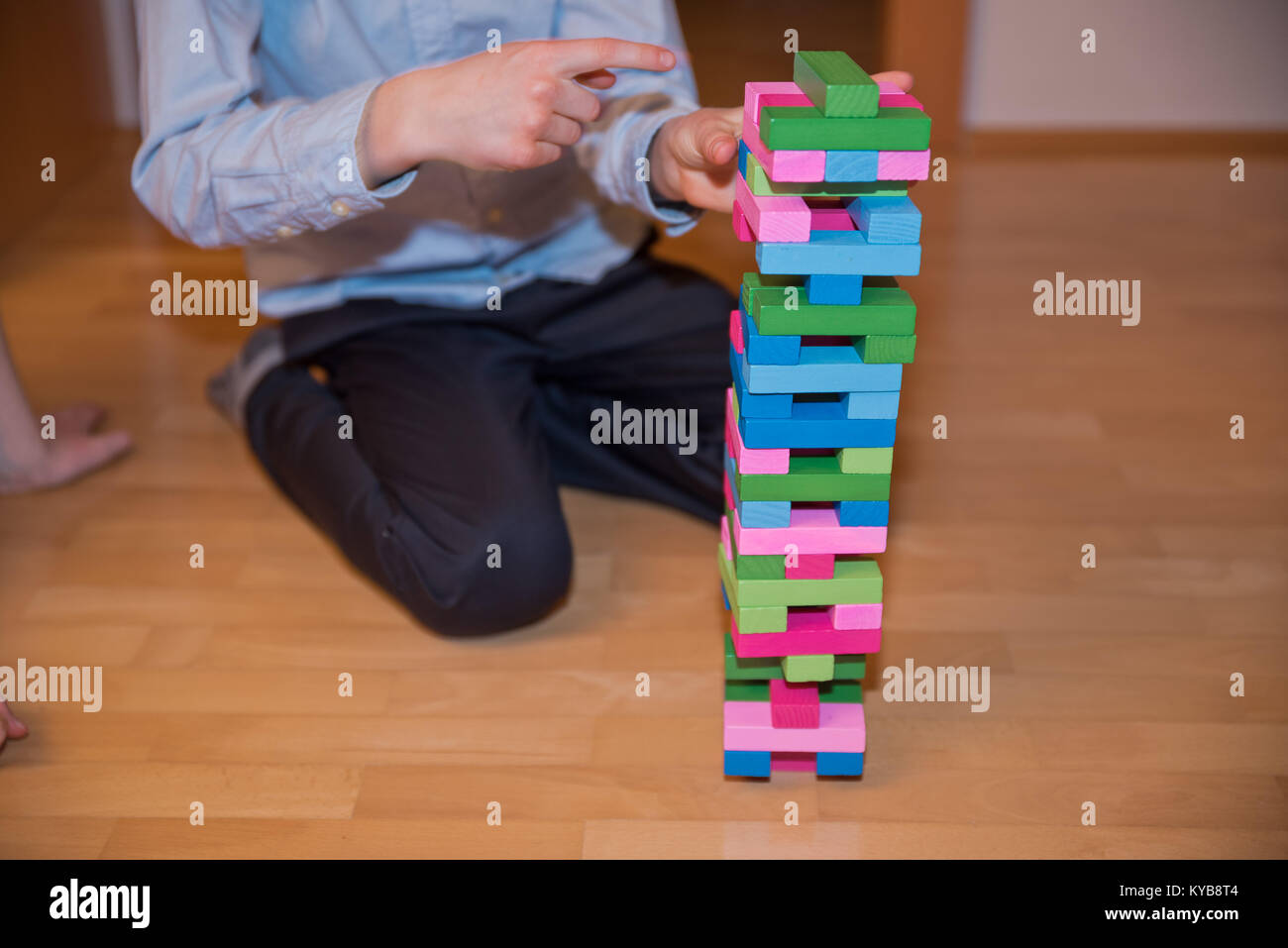 Child trying to take out a component of a colorful Jenga aka Klodsmajor parlor game, a social game in which you build a tower of wooden pieces until i Stock Photo