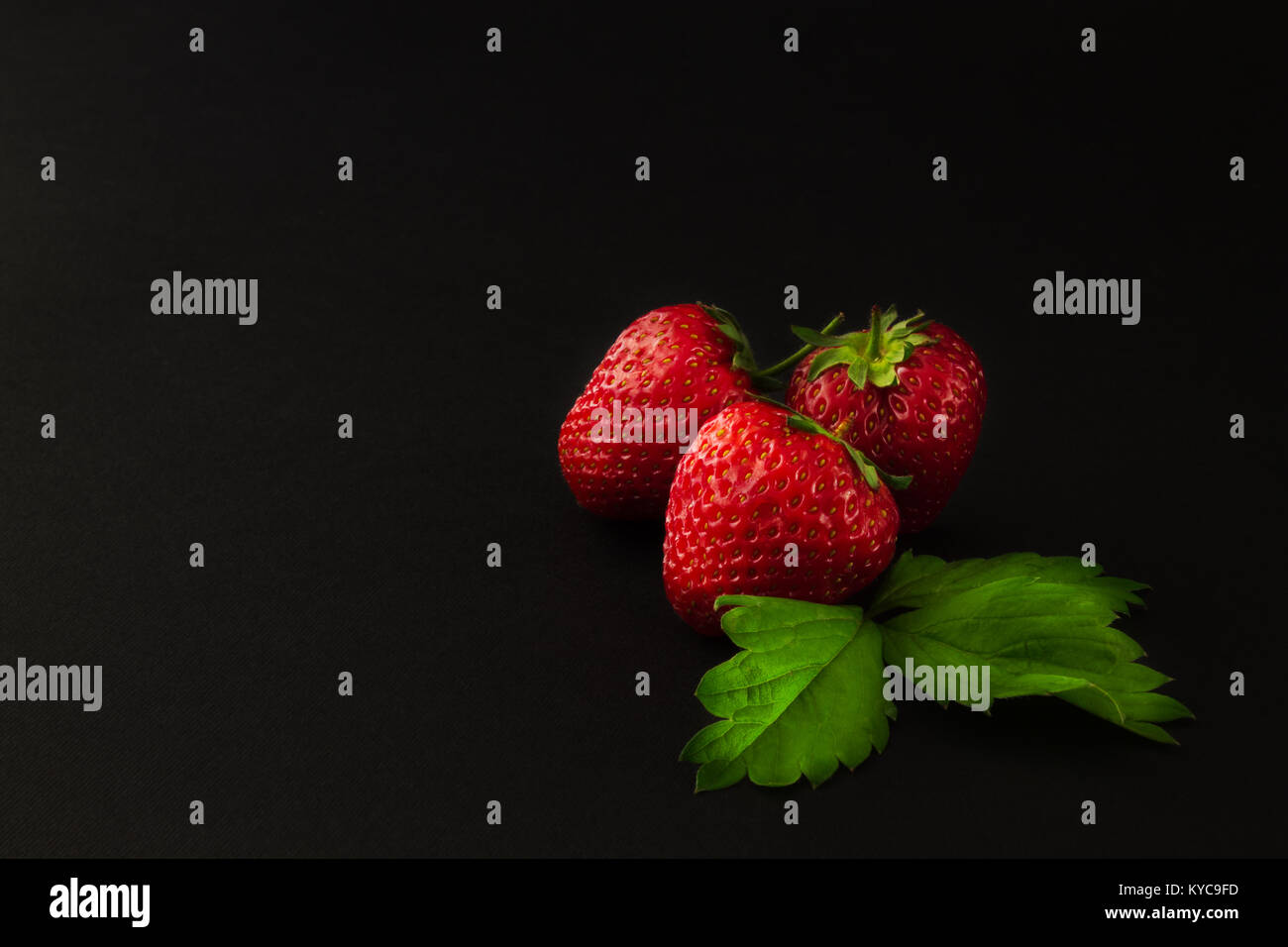 three ripe strawberries with leaves on a dark textural background Stock ...