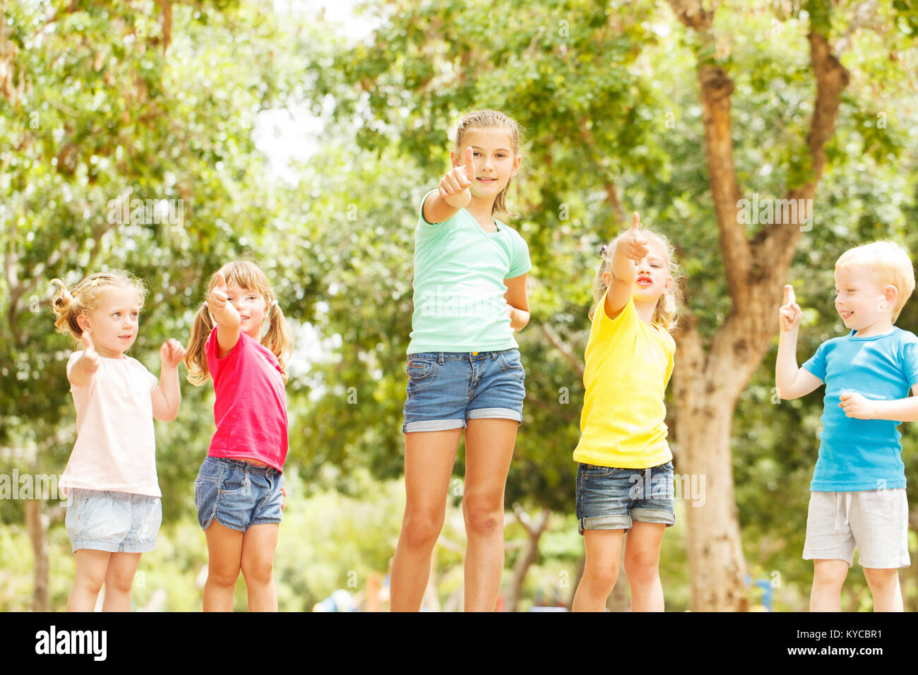 Group of happy children showing thumbs up outside Stock Photo