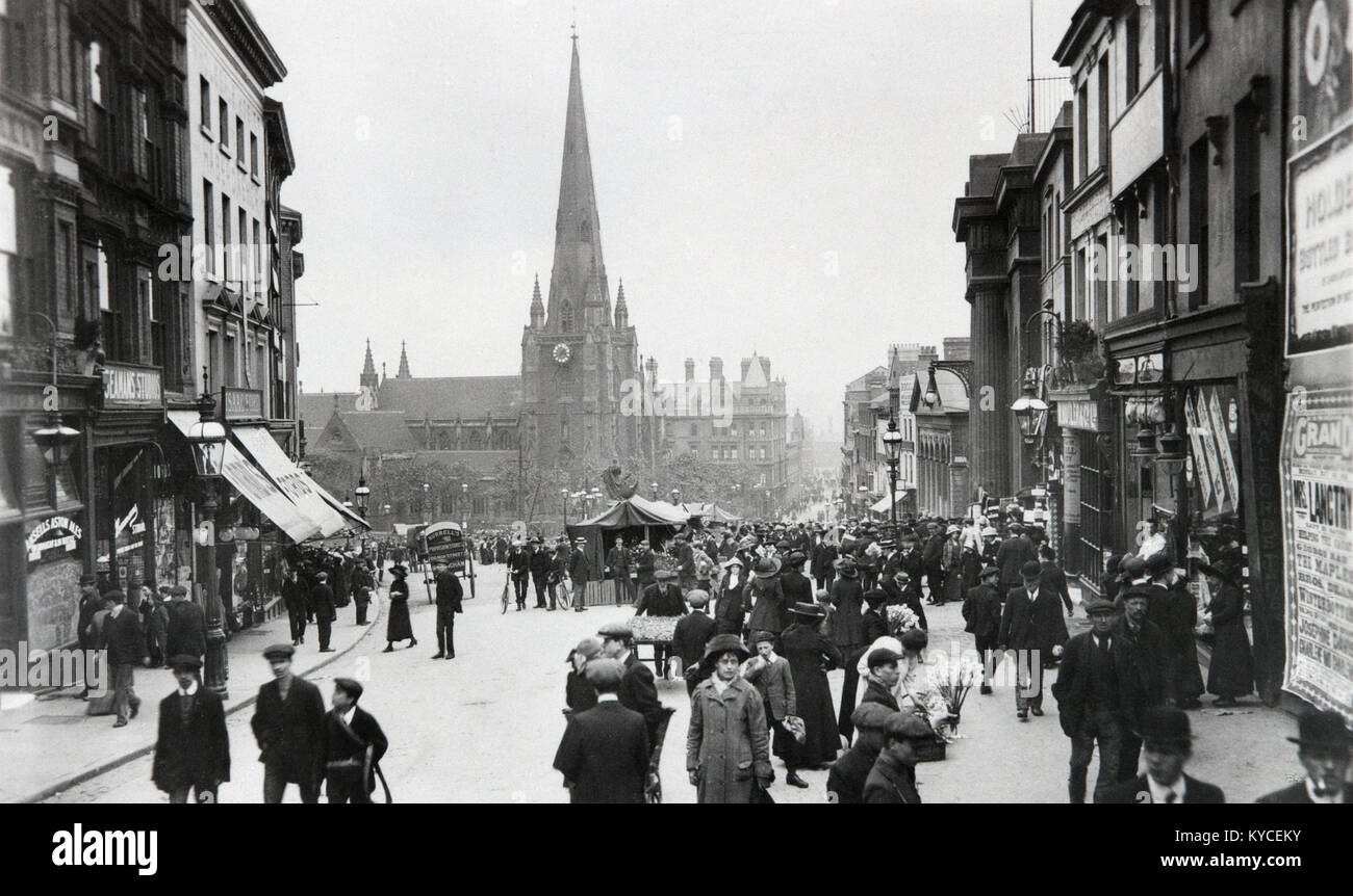 The High Street, Bull Ring in Birmingham, England. Date unsure, but early 20th Century, showing people, fashion, and shops of the era. A scene very reminiscent of the TV Series Peaky Blinders. The church of St. Martin in the background. Stock Photo