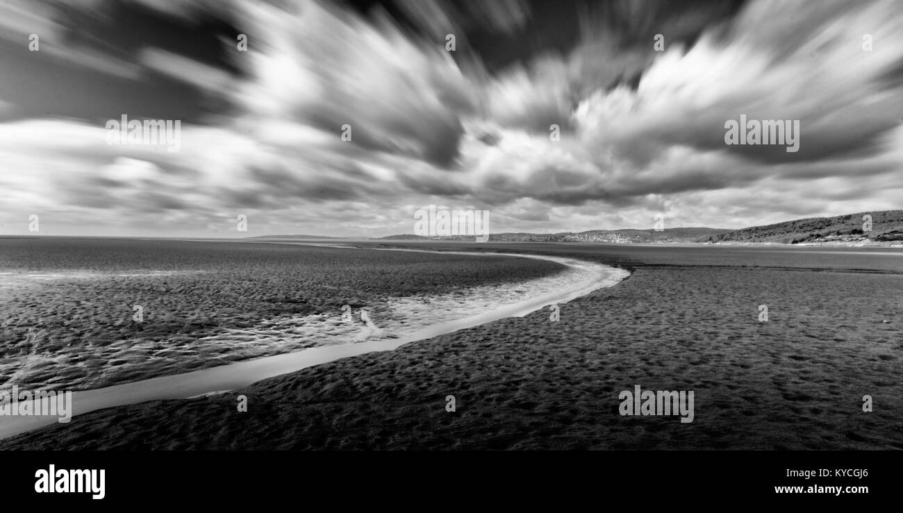A black and white long exposure photograph of the sands and sky around Arnside and Morcambe Bay Lancashire. There is movement in the dramatic clouds. Stock Photo