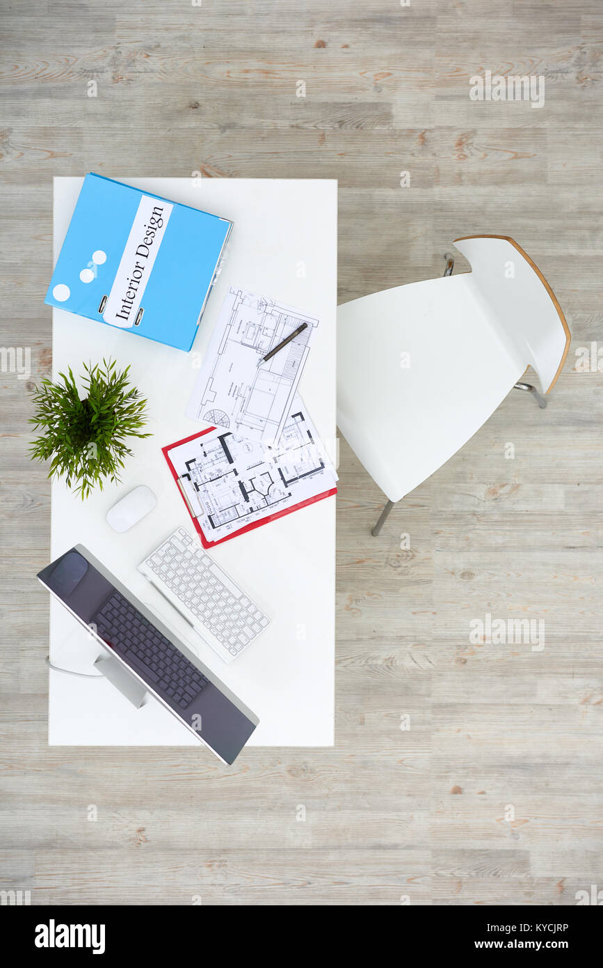 Modern studio of interior designer: wooden desk with floor plans, computer and folder, directly above view Stock Photo