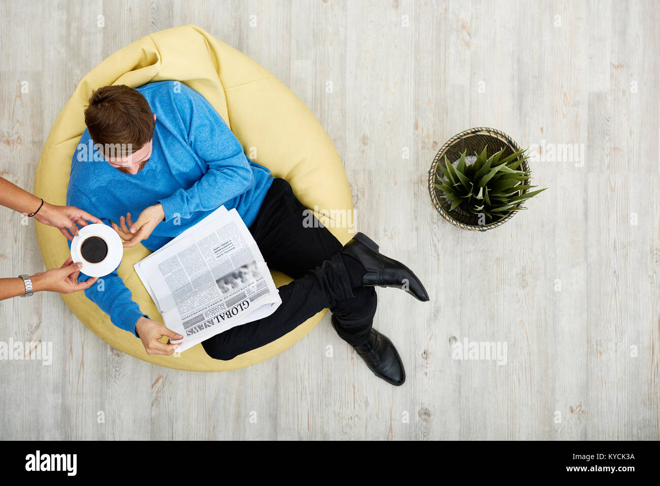 Bearded young man sitting on cozy beanbag chair and reading newspaper ...