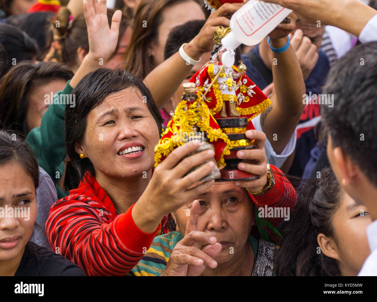 Cebu City, Philippines. 14th January, 2018.An expression of happiness as this woman holds out her Santo Nino figurine which is doused with Holy water by a priest,her face also dripping with Holy water.As part of the Sinulog 9 day religious festival,Filipino Catholics gather for early morning Sunday mass bringing with them Santo Nino figurines,replicas of the child Jesus.The belief in this Effigy dates back to the time of explorer Ferdinand Magellan who gave the original figurine as a gift when he landed in 1521 at Cebu. Credit: imagegallery2/Alamy Live News Stock Photo