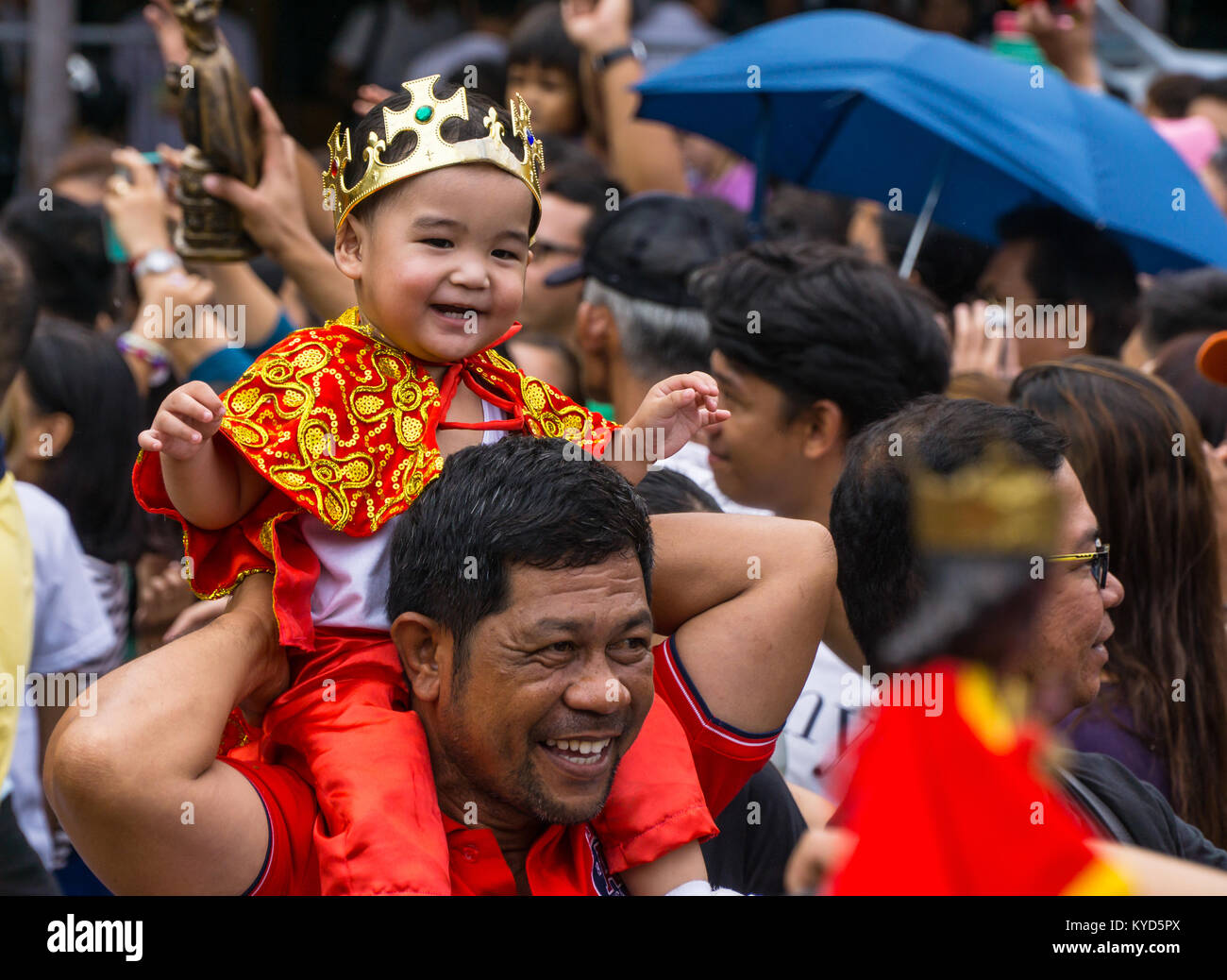 Cebu City, Philippines. 14th January, 2018. A happy smiling child dressed in a Santo  Nino outfit as he sits upon his fathers shoulders.As part of the Sinulog 9 day religious festival,Filipino Catholics gather for early morning Sunday mass bringing with them Santo Nino figurines,replicas of the child Jesus.The belief in this Effigy dates back to the time of explorer Ferdinand Magellan who gave the original figurine as a gift when he landed in 1521 at Cebu. Credit: imagegallery2/Alamy Live News Stock Photo