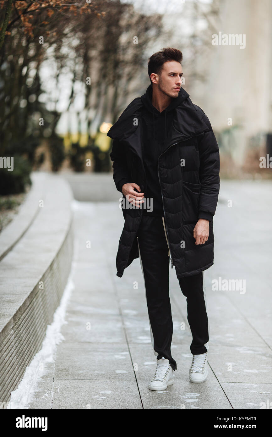 Stylish man wolk on the street. Winter cold outfit. Big jacket with white  sneakers. Blured background street. Profecional model photo Stock Photo -  Alamy