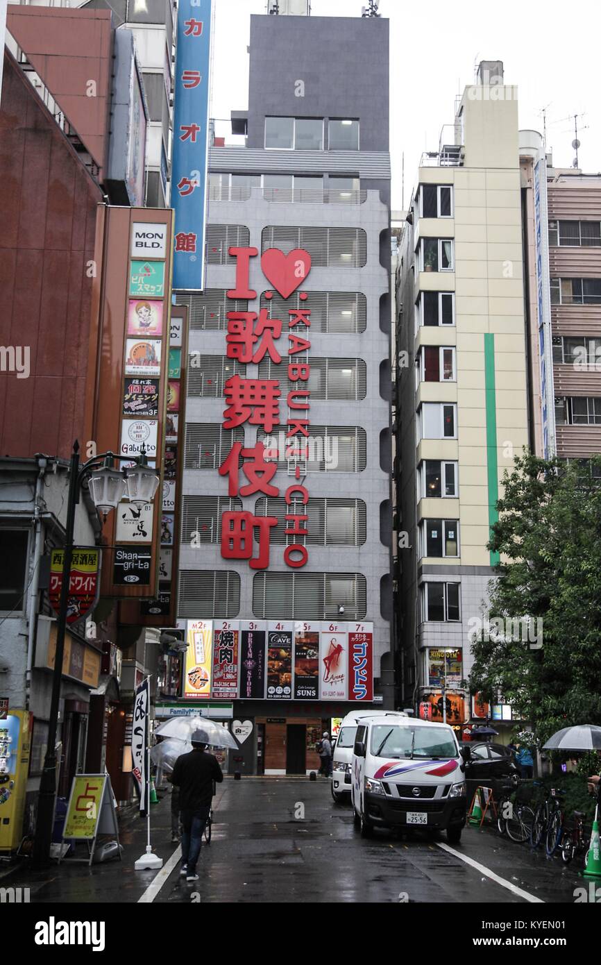 People holding umbrellas walk past a sign in Japanese and English reading I Love Kabukicho, in the Kabukicho Red Light District, Shinjuku, Tokyo, Japan, October 16, 2017. () Stock Photo