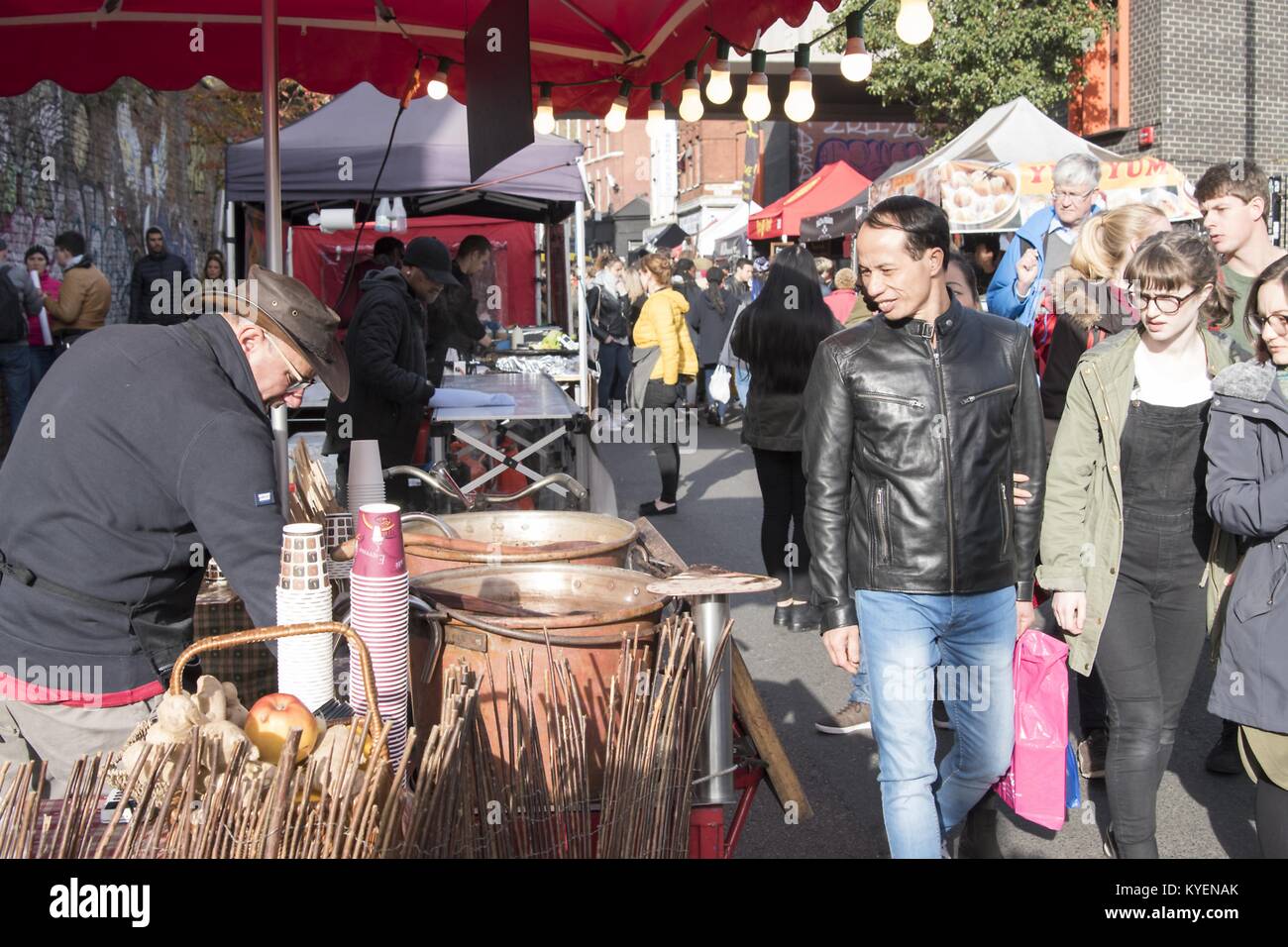 Millennial generation visitors look on as a man cooks street food at the Brick Lane Market, a major shopping district and outdoor market for secondhand goods in Tower Hamlets, East London, United Kingdom, October 29, 2017. () Stock Photo