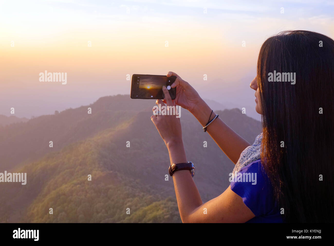A Indian young  women taking photograph of sunrise using a mobile phone rear camera. Stock Photo