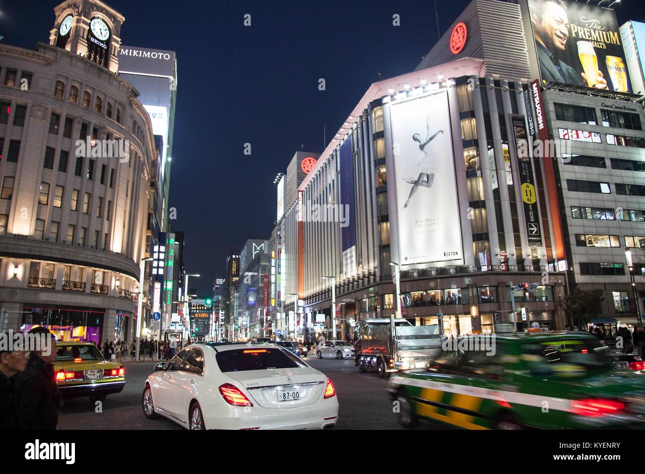 Cars pass through a busy intersection as pedestrians prepare to cross, with brightly lit shops and billboards visible, at night in the Yurakucho Ginza district, known for its older restaurants and bars, in the Chiyoda Ward of Tokyo, Japan, November, 2017. () Stock Photo