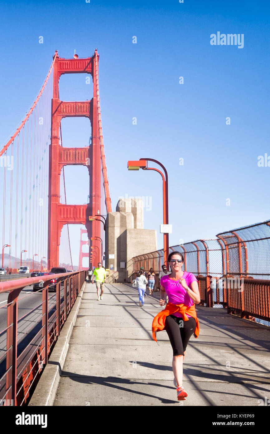 SAN FRANCISCO, CA- Oct. 11, 2015: Golden Gate Bridge runner, in an orange jacket that matches the bridge's famous color. Sunny day in San Francisco. C Stock Photo