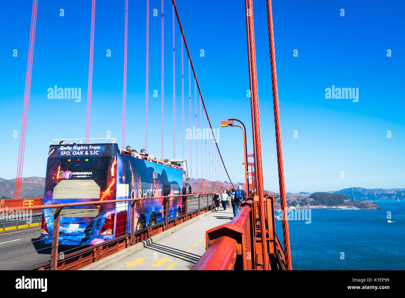 SAN FRANCISCO, CA - OCT 11, 2015: Double decker tour bus driving on the Golden Gate Bridge and people on the pedestrian walkway. Sunny day with blue s Stock Photo