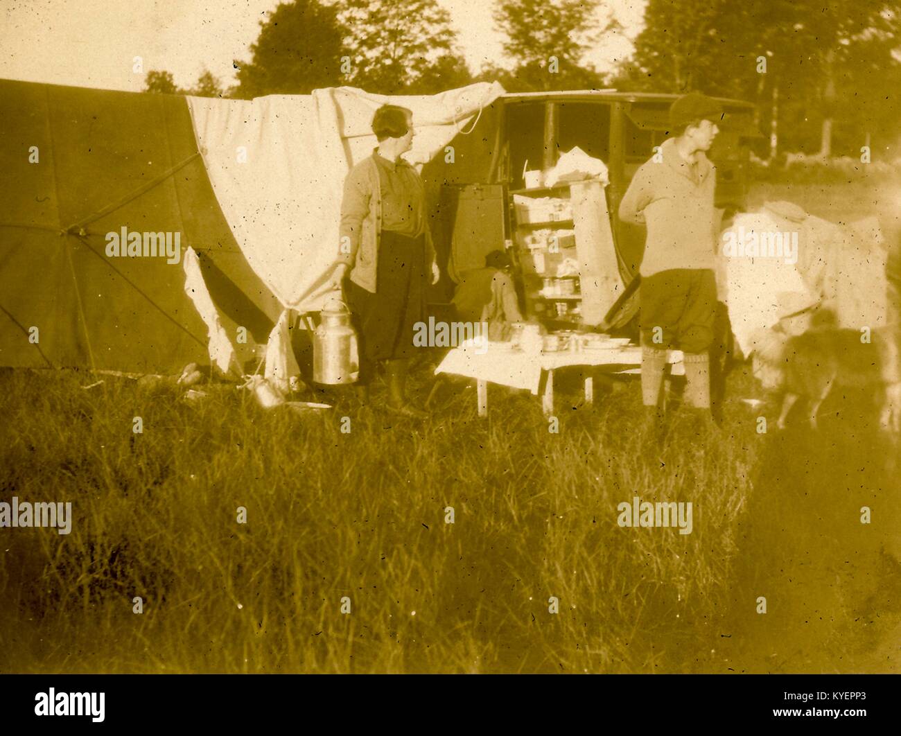 A man and woman stand at their campsite, with a tent and their automobile visible, a variety of food items in the foreground, in New Hampshire during a road trip through New England, 1925. () Stock Photo