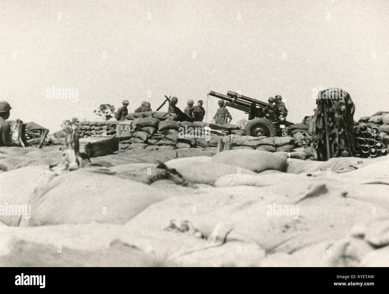 American servicemen stand in a foxhole surrounded by sandbags and operate an artillery cannon during the Vietnam War, 1968. () Stock Photo