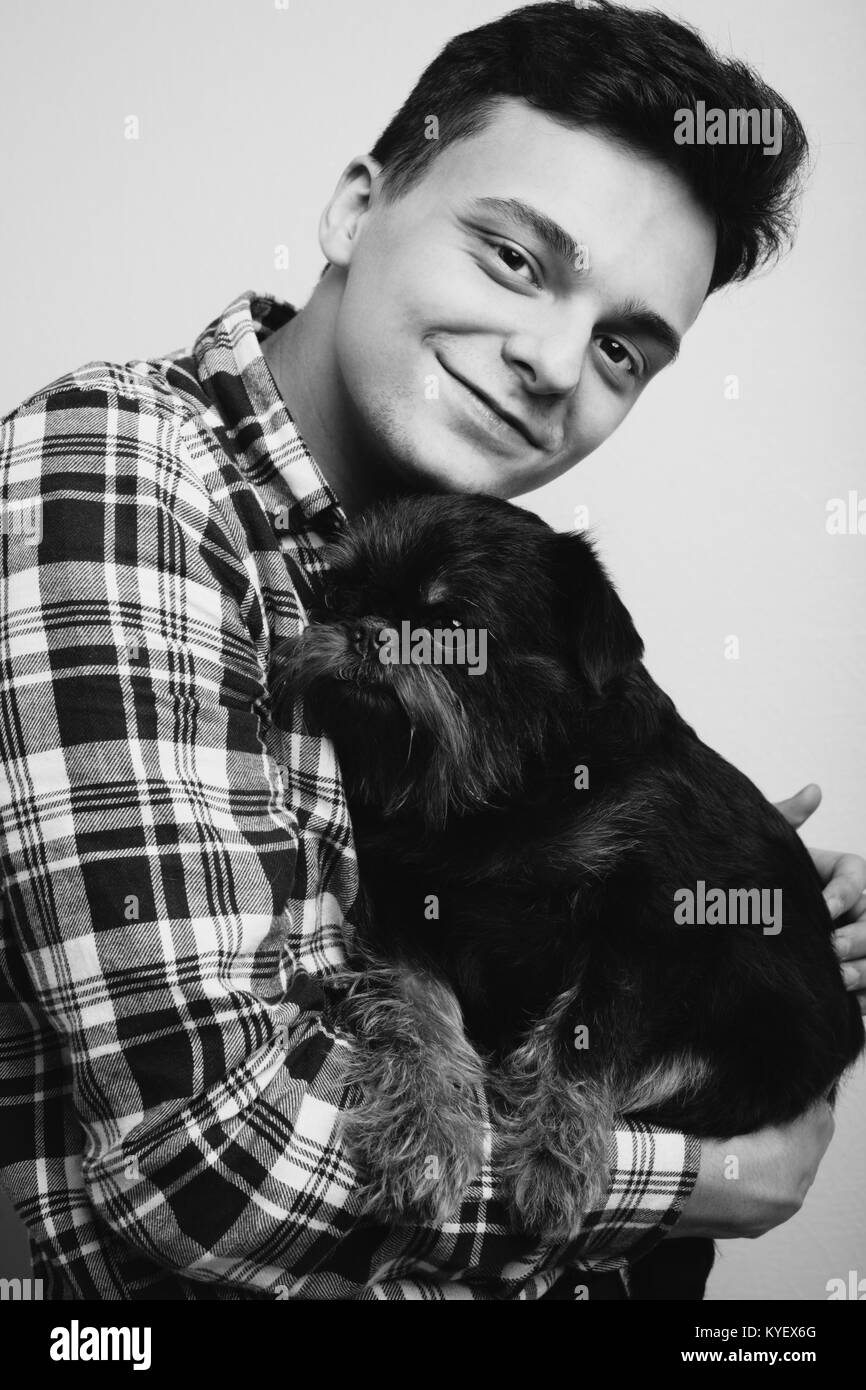 Closeup portrait handsome young hipster man, kissing his good friend black dog isolated light background. Positive human emotions, facial expression, feelings. Black and white photo Stock Photo