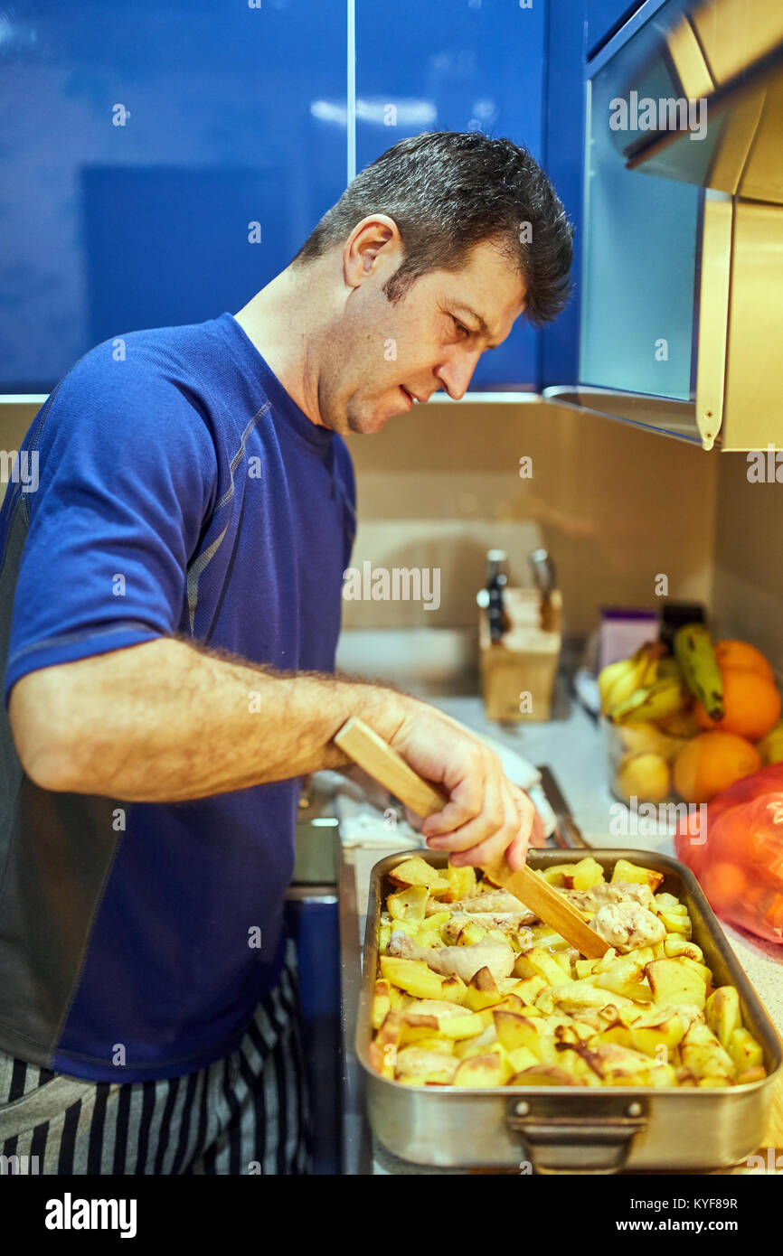 Middle aged man cooking at home chicken drums in an oven tray Stock