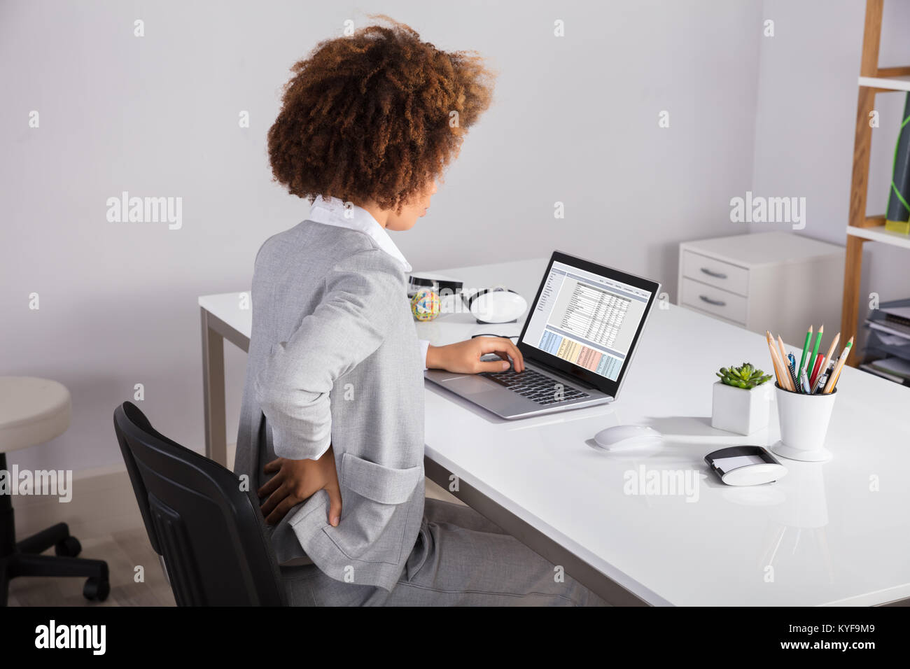 Businesswoman Holding Her Back While Working On Laptop At Office Desk Stock Photo