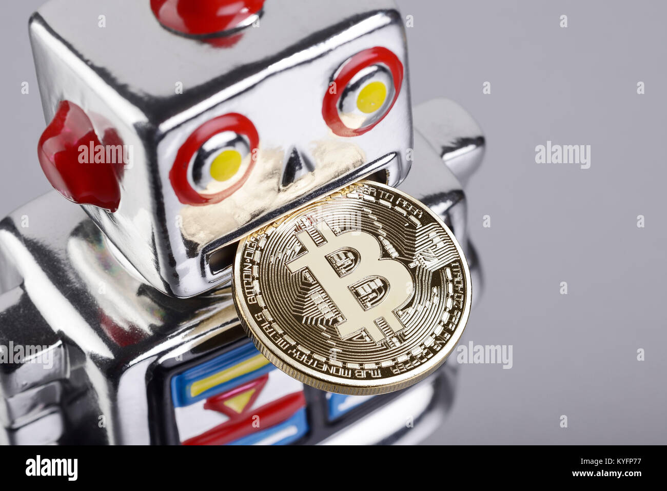Silver robot shaped money box eating a bitcoin coin Stock Photo