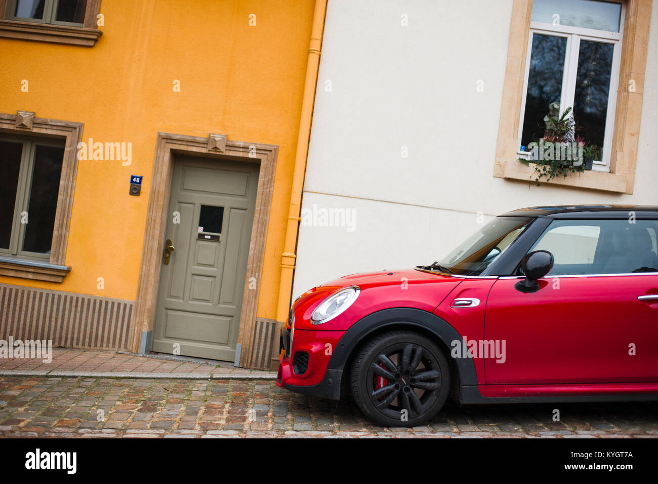 Modern, red car parked in front of historic, yellow house. Luxembourg Stock Photo