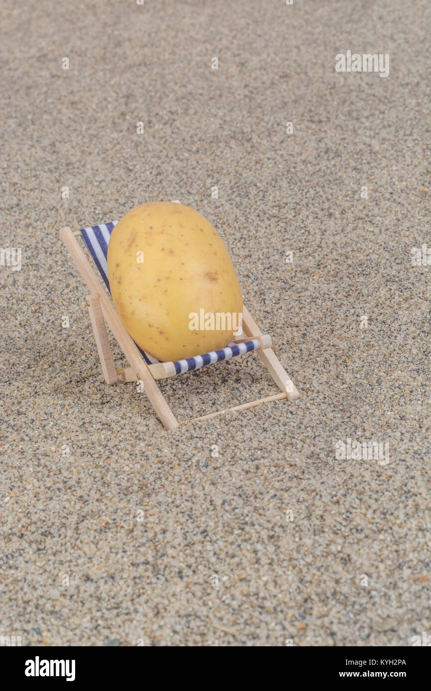 New potato on toy deckchair on sand as visual metaphor for concept of