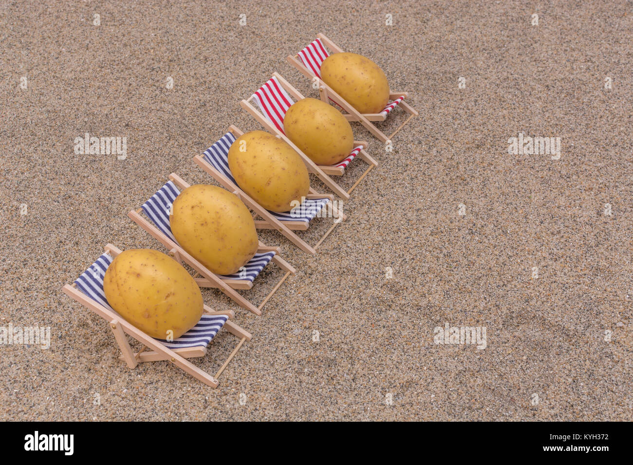 New potatoes on toy deckchairs on sand as visual metaphor for concept