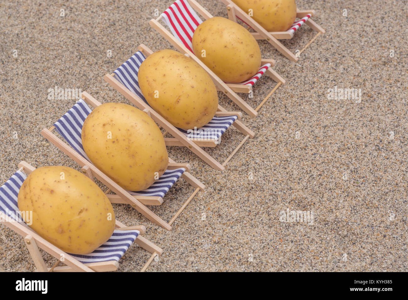 New potatoes on toy deckchairs on sand as visual metaphor for concept