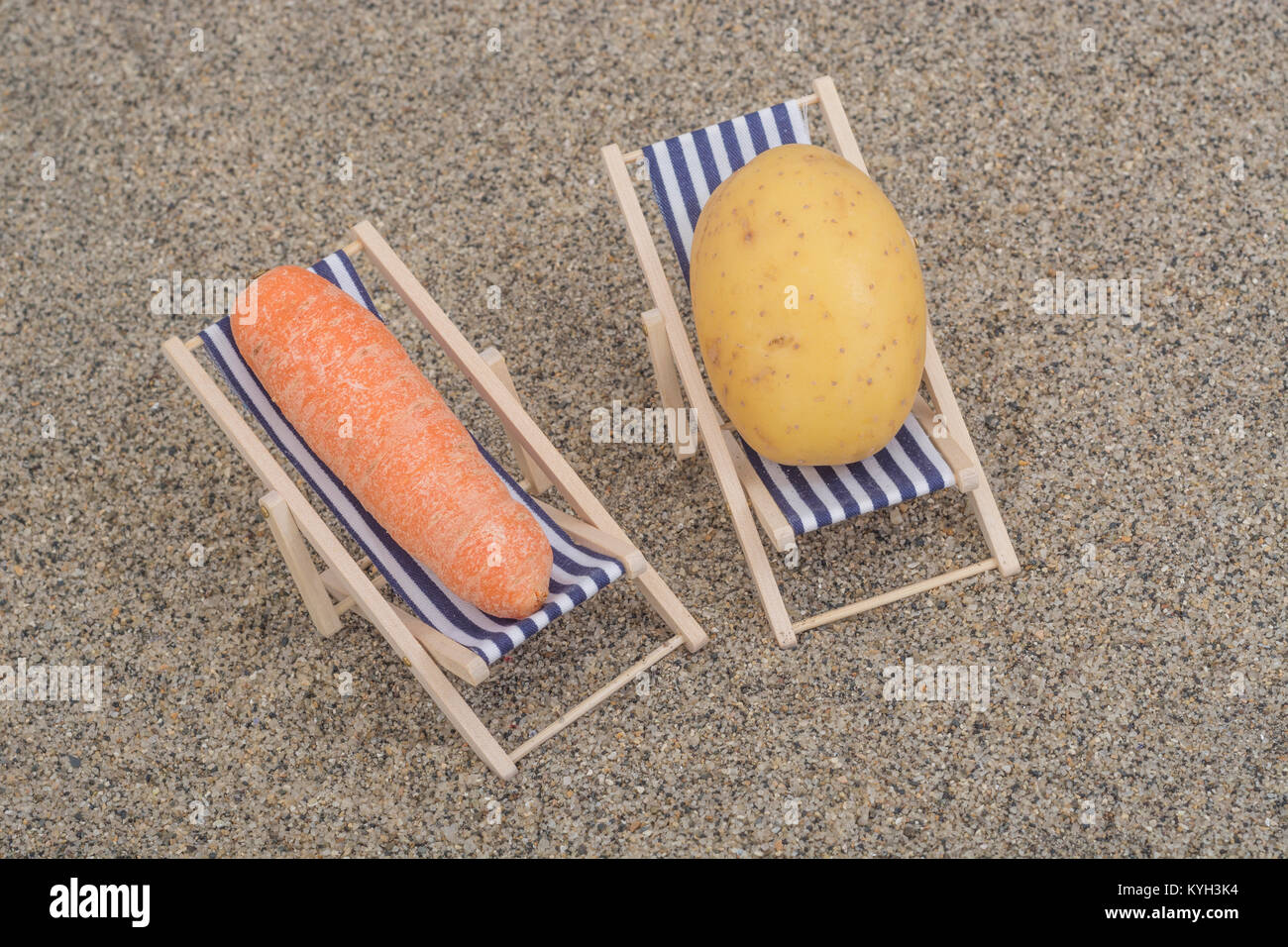 New potato and small carrot on toy deckchairs on sand as visual