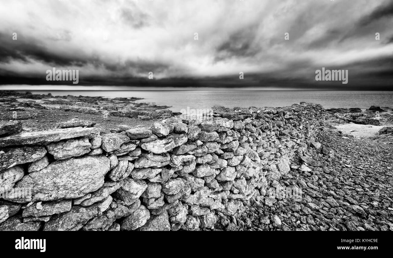 Faro, Sweden, Baltic Sea island, dramatic rocky coast with old stone wall to the water. Black and white monochrome. Moody sky. Stock Photo