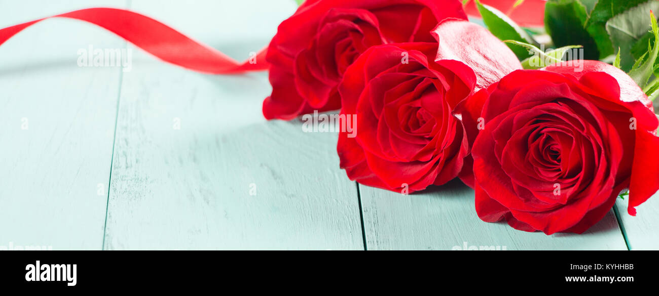Three fresh red roses with a red ribbon on a aquamarine table Stock ...