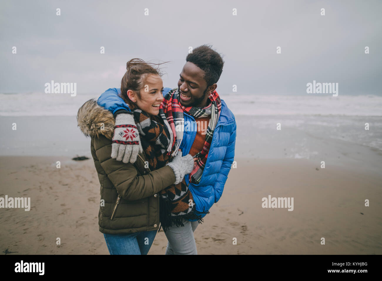 A young couple take a romantic stroll along a winter beach with their arms around each other. Stock Photo