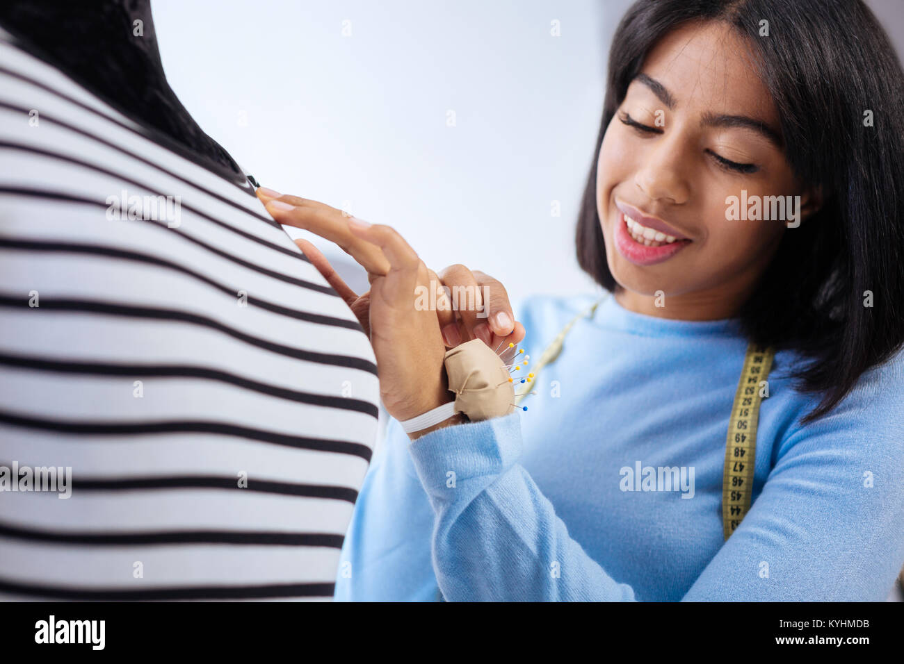 Smiling woman taking a little pin for a blouse while working Stock Photo